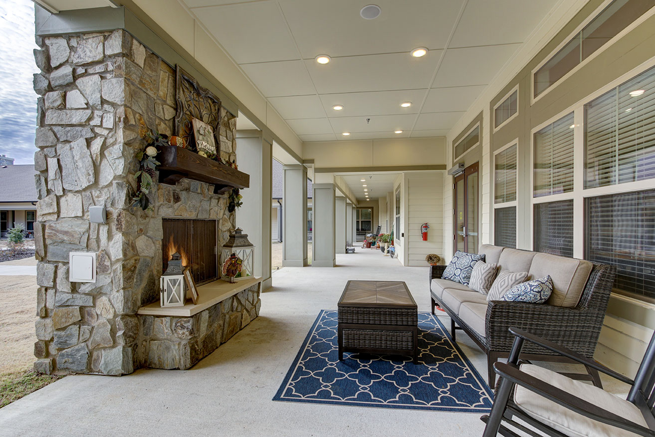 Covered outdoor patio at Ridgemere Senior Living with stone fireplace, cushioned seating, and a relaxing space for residents to gather year round.