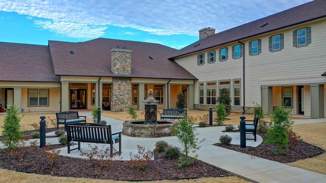 Courtyard at Ridgemere Senior Living featuring a central fountain, benches, landscaped walkways, and outdoor seating surrounded by the community.