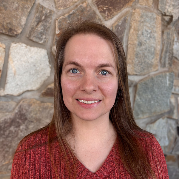 Ashley Thomas, Wellness Director at Ridgemere Senior Living, smiling while wearing a textured red top, standing in front of a natural stone wall background.
