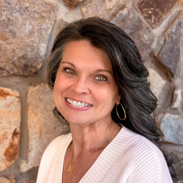 Brandy Herrin, Senior Living Director at Ridgemere Senior Living, smiling while wearing a light sweater and gold hoop earrings, standing in front of a stone wall background.