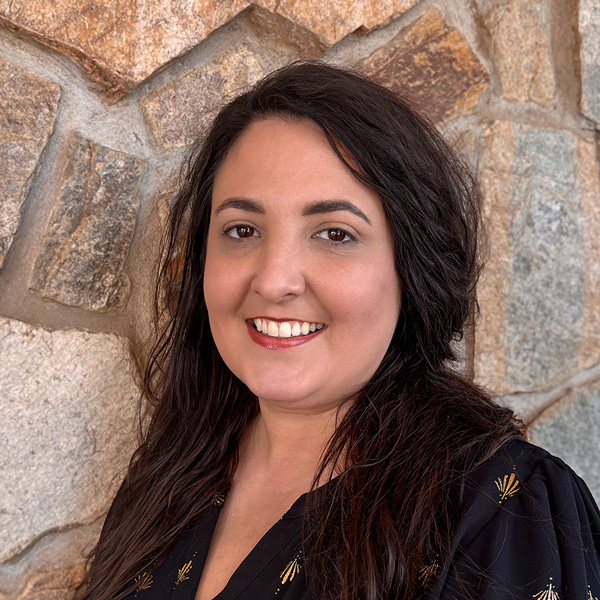 Jessica Adams, Business Office Director at Ridgemere Senior Living, smiling while wearing a black blouse with subtle gold details, standing in front of a natural stone wall background.