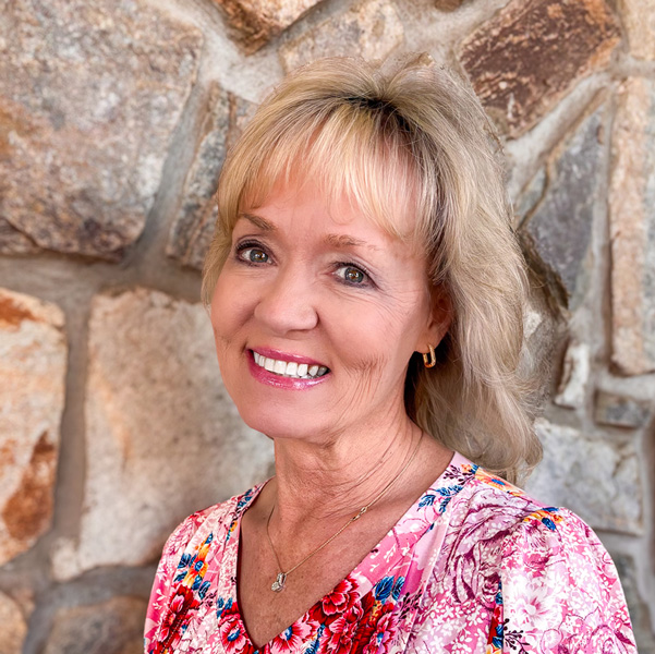 Sherri Newton, Executive Director at Ridgemere Senior Living, smiling warmly while wearing a pink floral blouse, standing in front of a stone wall background.