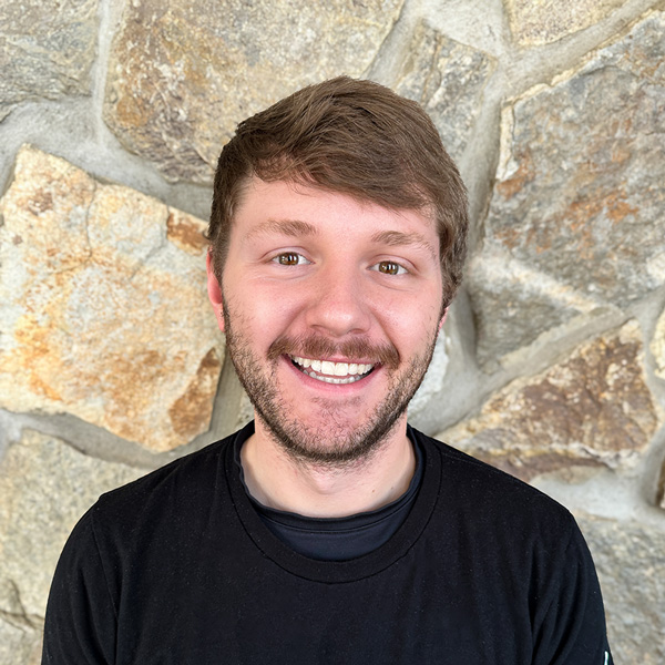 Chase Wilson, Culinary Director at Ridgemere Senior Living, smiling in front of a natural stone wall, wearing a black shirt.