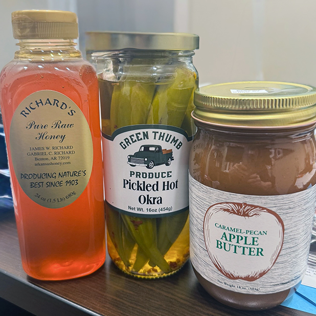 A selection of delicious products offered by a local business, including honey, pickled okra, and caramel-pecan apple butter.