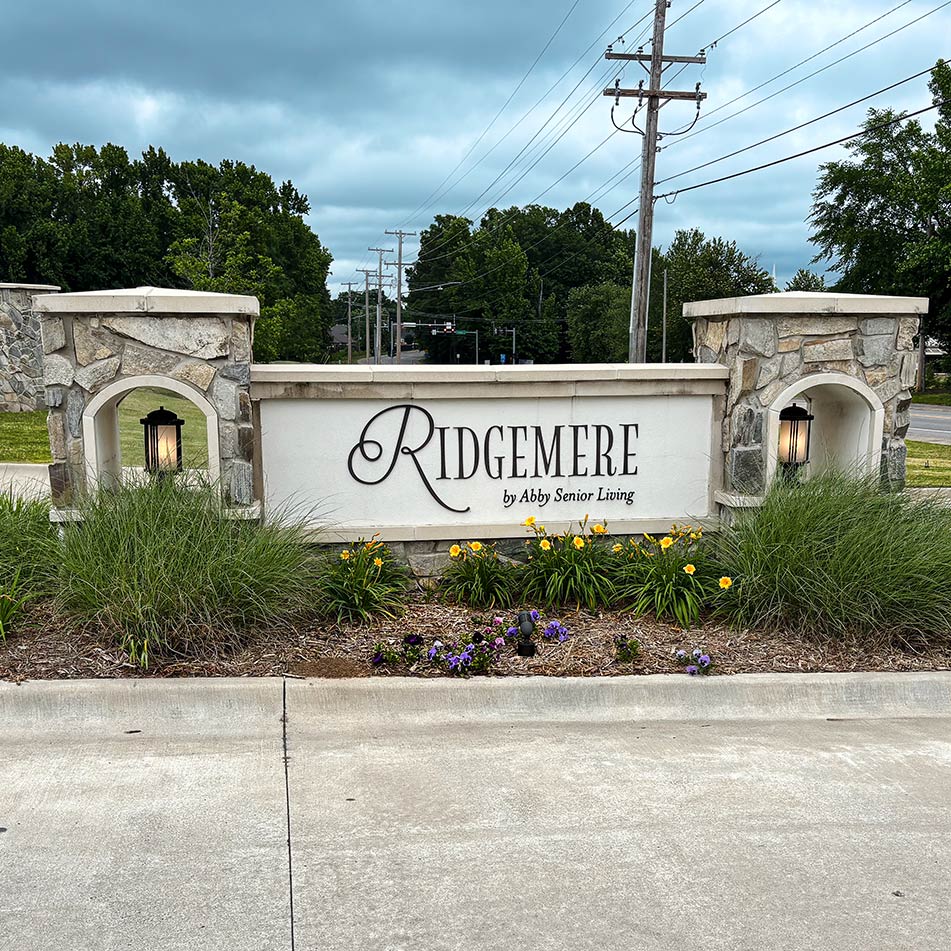 The exterior sign at Ridgemere Senior Living, bookended with stone and lanterns, landscaped beautifully.